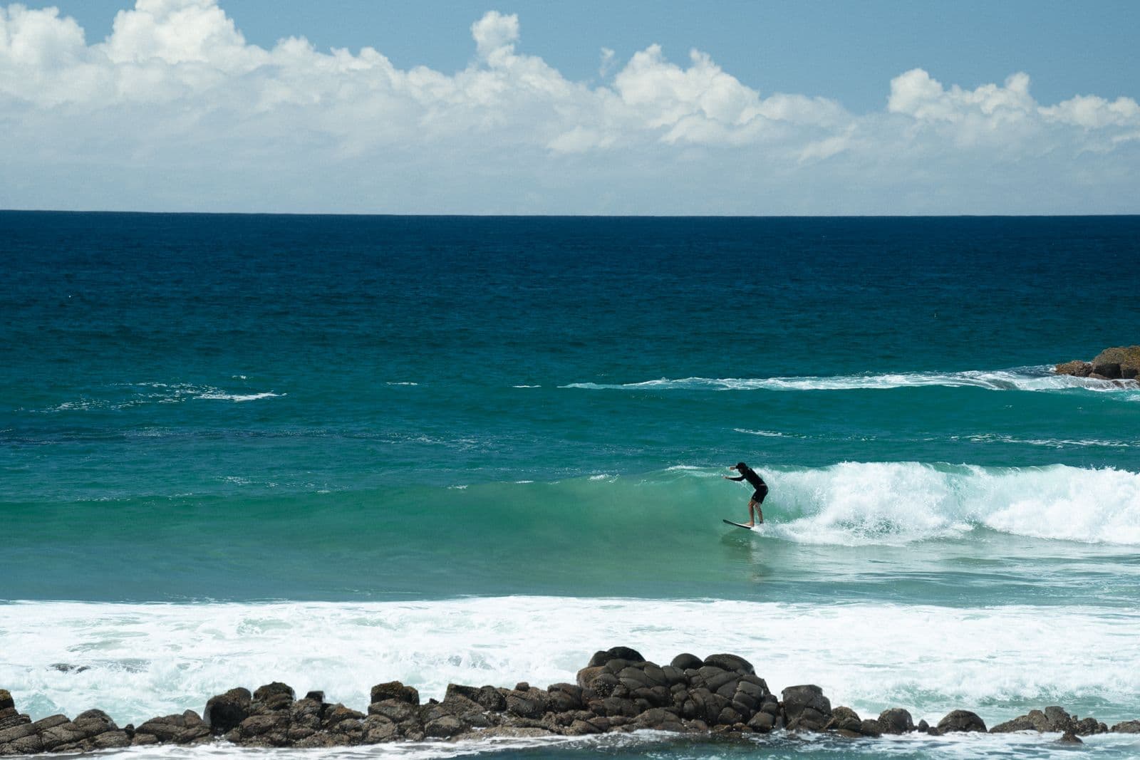 A surfer riding a small clean wave on a sunny beach