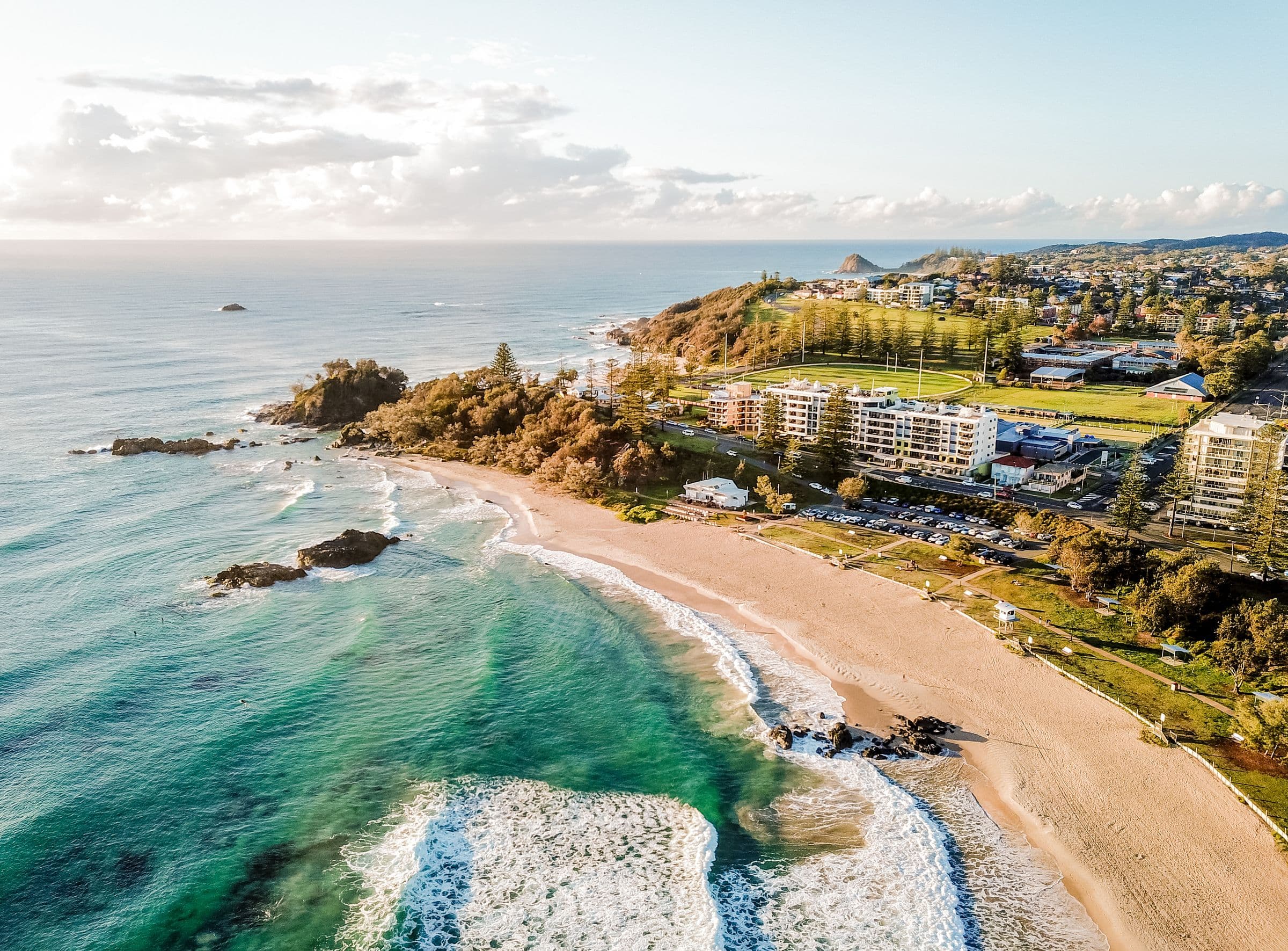 Aerial view of Port Macquarie's Town Beach, with surf breaking on golden sand and Norfolk pines along the foreshore